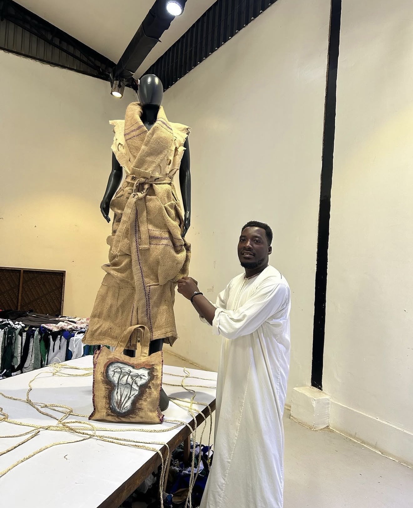 Mukasa Najib, Bobbin Case designer, standing with a sisal sack dress on a mannequin in his studio, Uganda