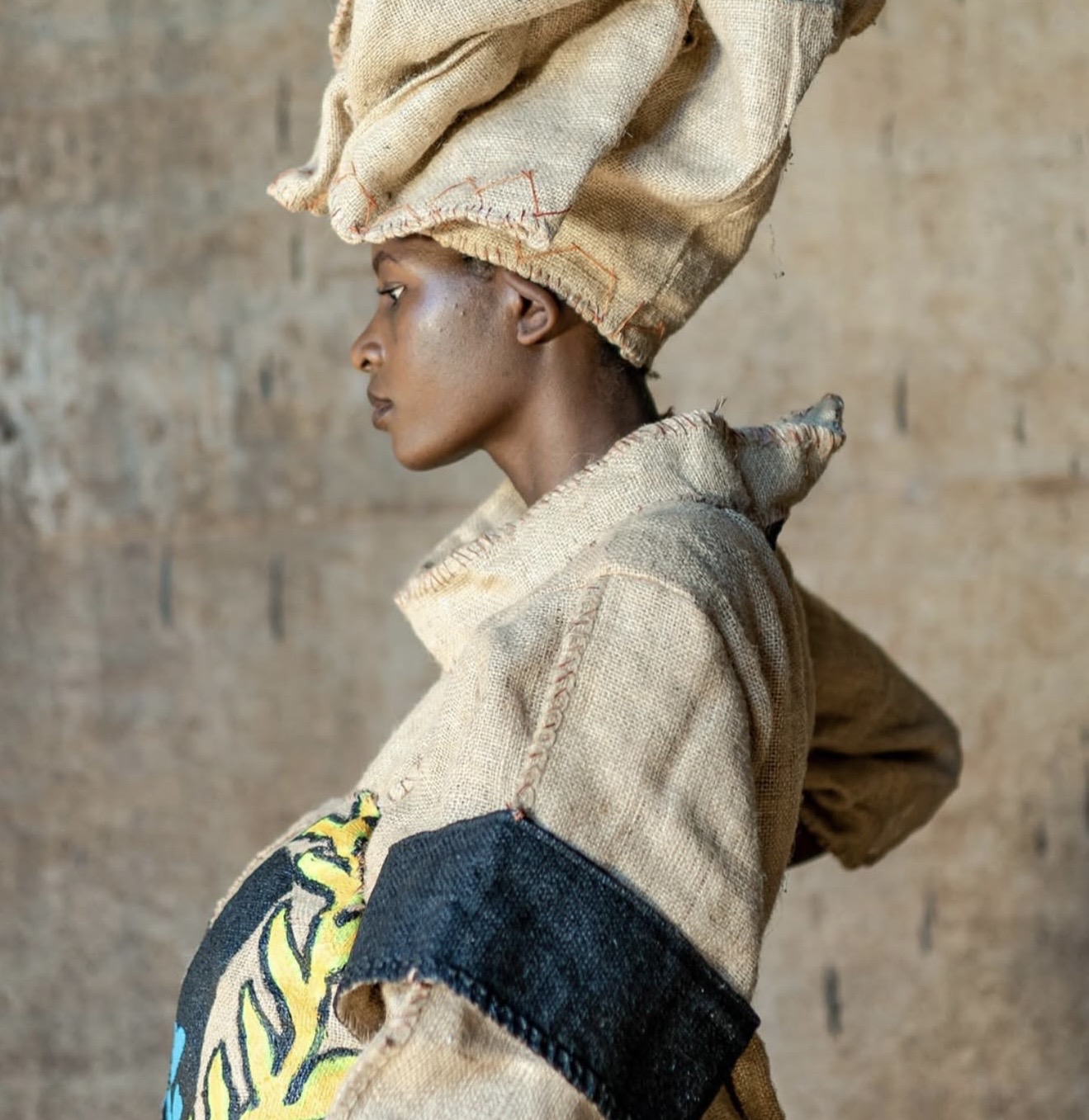 Model wearing painted sisal sack coat with hand-painted artwork depicting social commentary — editorial shoot, Uganda