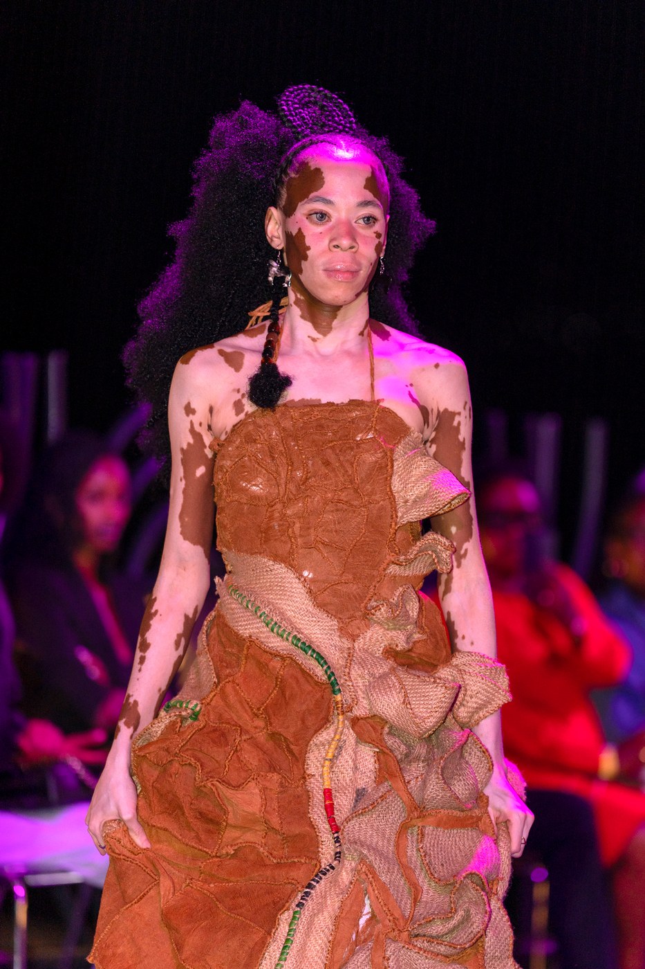 Model in strapless rust and sisal ruffle gown walking the Bobbin Case runway at Kigali Fashion Week 2026 under pink stage lighting